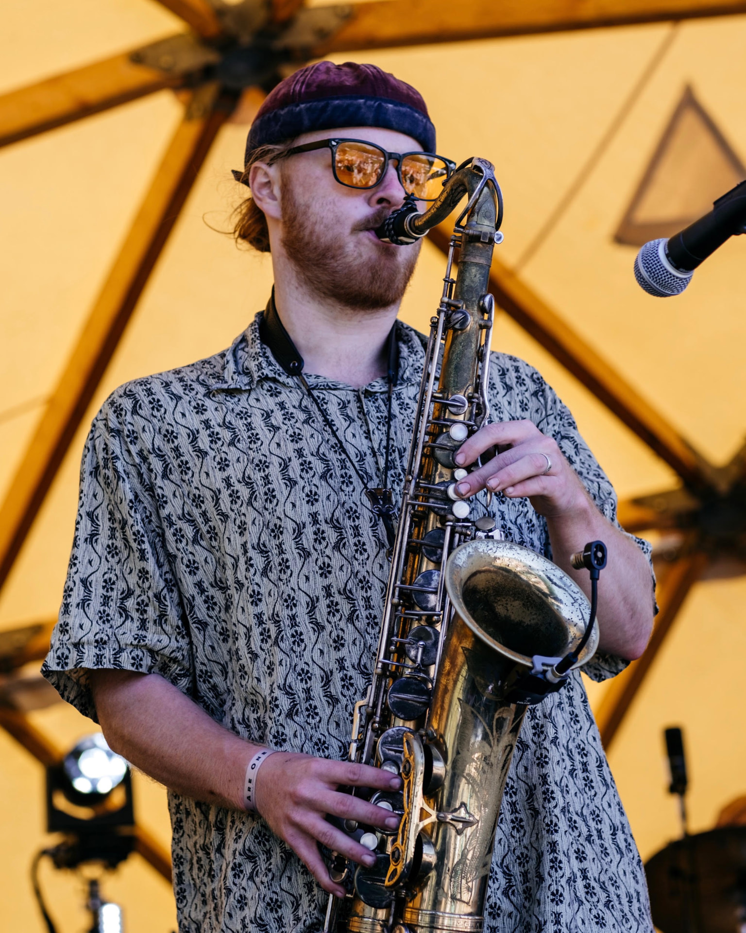 Saxophone player in a patterned shirt performing in the golden daylight tent