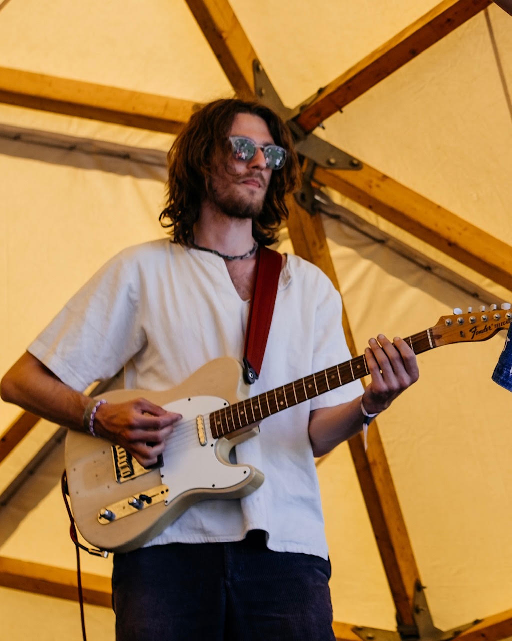 Guitarist with a white Telecaster playing under the sunlit tent canopy